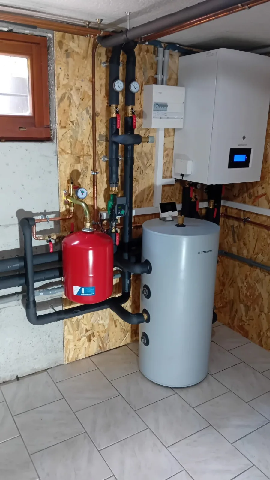 Vue d'ensemble du local technique à Achenheim : module intérieur de la pompe à chaleur air-eau fixé au mur, ballon posé au sol et vase d'expansion.