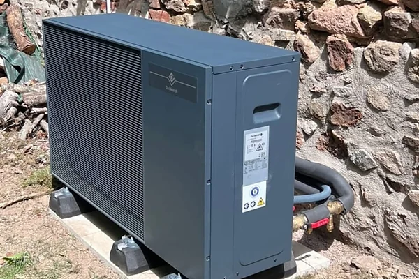 Unité extérieure d'une pompe à chaleur air-eau installée récemment par Rexer Energies, posée sur socle béton le long d'un mur en pierre.